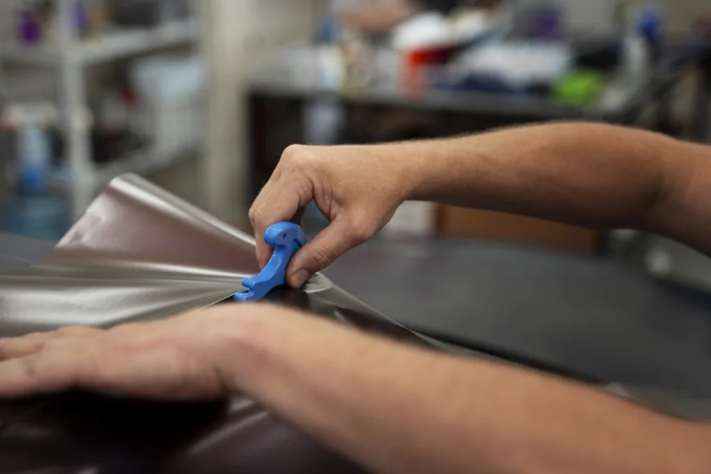 Close-up of a hand applying silver vinyl wrap with a blue squeegee tool