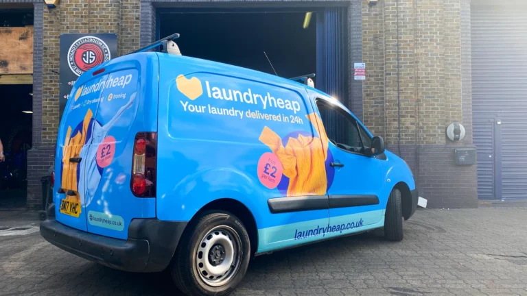 Laundry service van with a blue Custom Van Wrap featuring clothing graphics, contact details, and a bold logo, creating a professional and eye-catching mobile advertisement for the business.