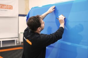 A professional wrap installer applying a white vehicle wrap to the side of a black truck at WrapMates.