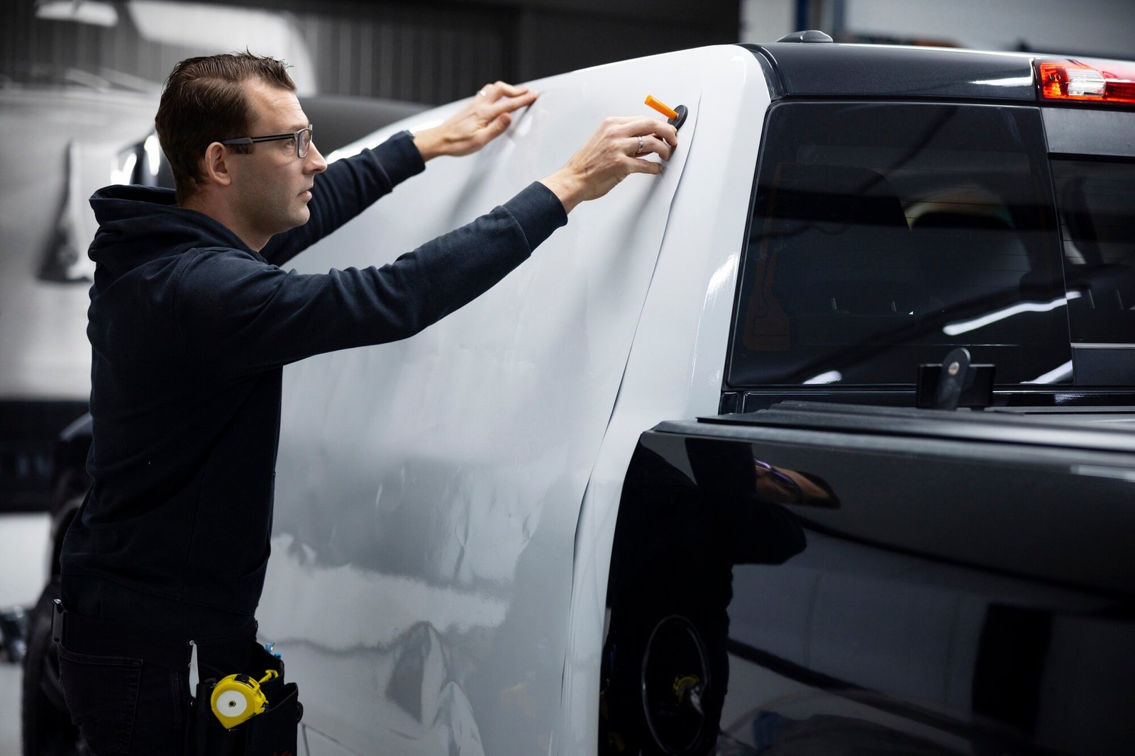 A professional wrap installer applying a white vehicle wrap to the side of a black truck at WrapMates.