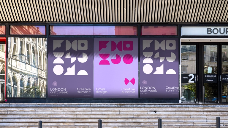 Three large, modern, geometric posters displayed in a storefront window advertising "LONDON craft week," "Creative summit," and "Cover design." The posters use white and magenta abstract shapes on a purple background.