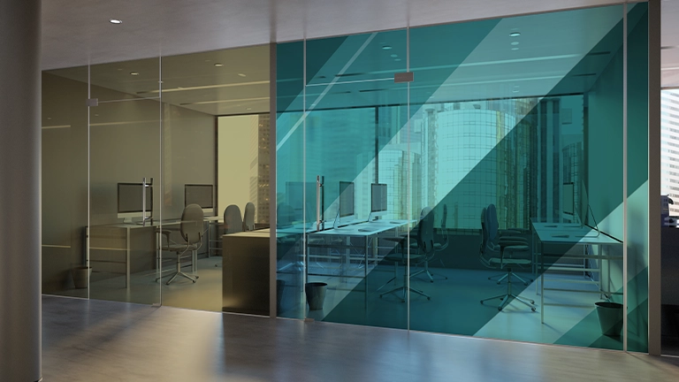 Interior office glass wall featuring two sections: one with a golden-yellow tint and another with a bright, diagonal teal-blue privacy film. Desks and computer monitors are visible through the glass