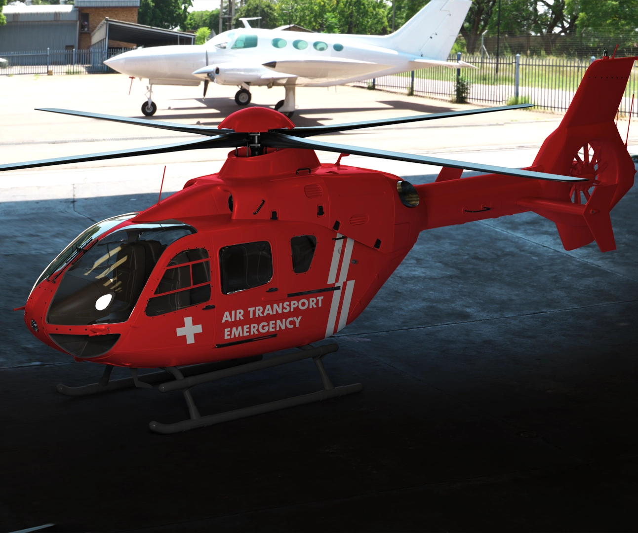 A bright red emergency response helicopter with "AIR TRANSPORT EMERGENCY" text and a white cross, parked in a hangar with a white plane in the background.