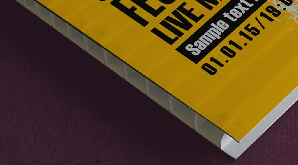A high-detail close-up of the edge of a yellow fluted corex board, showing the internal twin-wall "honeycomb" structure and printed event details.