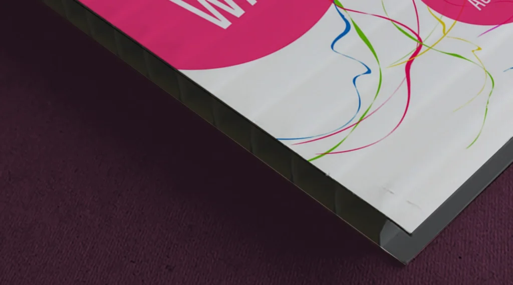 A high-detail close-up of the edge of a Dibond board, showing the solid black polyethylene core sandwiched between two thin aluminum sheets with a glossy white printed surface