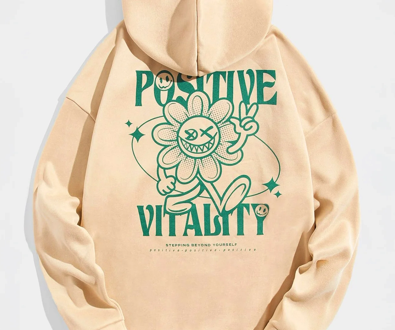 Rear view of a tan hoodie featuring a large green graphic of a smiling cartoon flower with a peace sign, framed by the words "POSITIVE VITALITY".