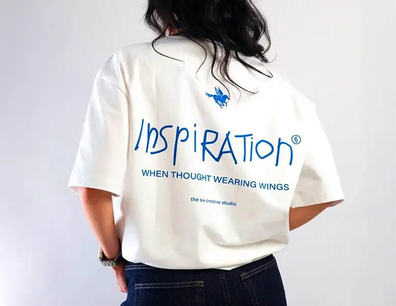 Rear view of a person wearing a white oversized t-shirt featuring blue "INSPIRATION" graphic printing.