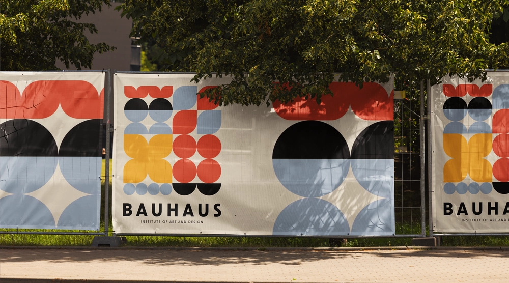 Large-format outdoor PVC mesh banners featuring "BAUHAUS Institute of Art and Design" geometric branding attached to a perimeter fence.