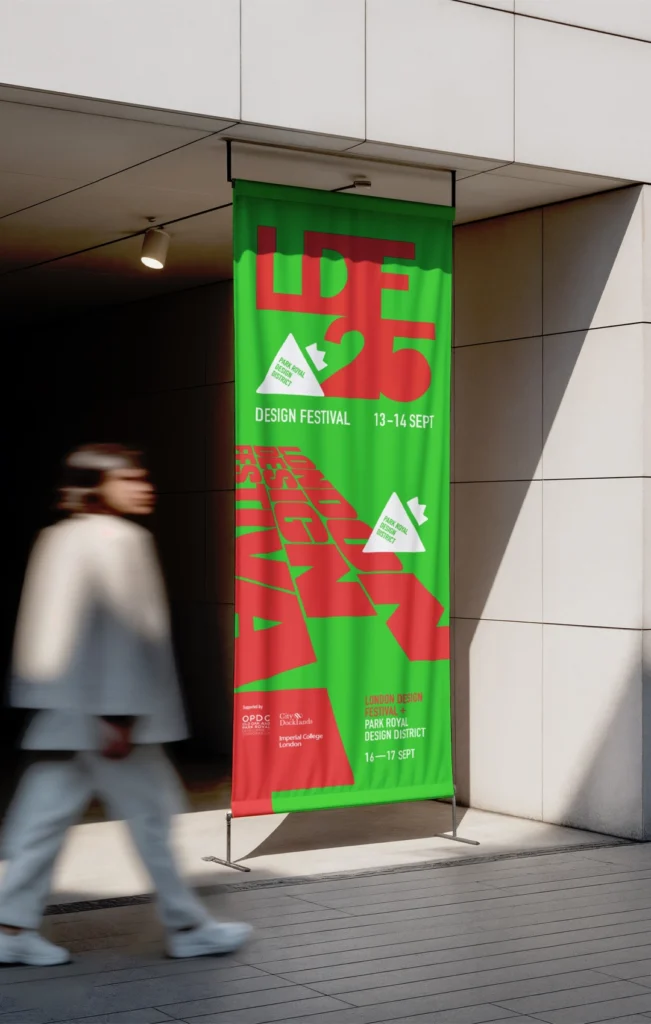 A tall vertical green PVC banner with bold red 'LDF 25' typography, mounted on a tensioned floor-to-ceiling stand at a building entrance.