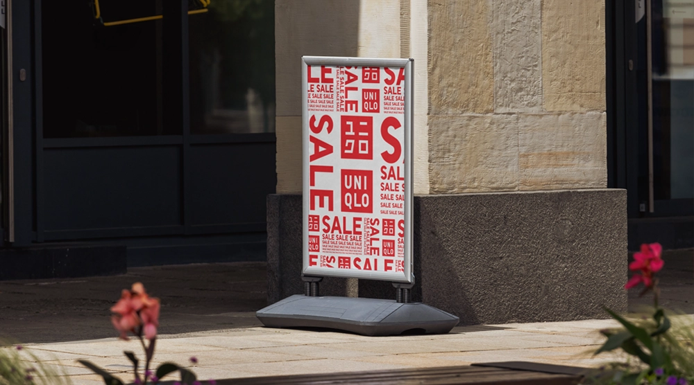 Outdoor sidewalk pavement sign with a large-format poster for "Natural Organic Coffee" in a silver spring-mounted frame.