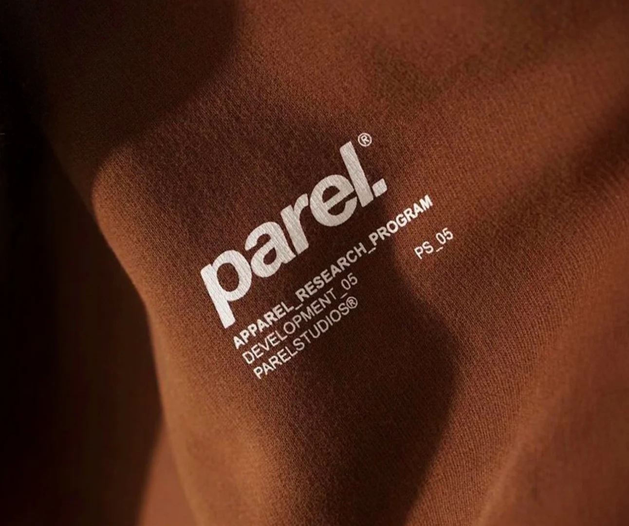 Close-up of brown textile material featuring a white printed "parel." logo and technical branding specifications.