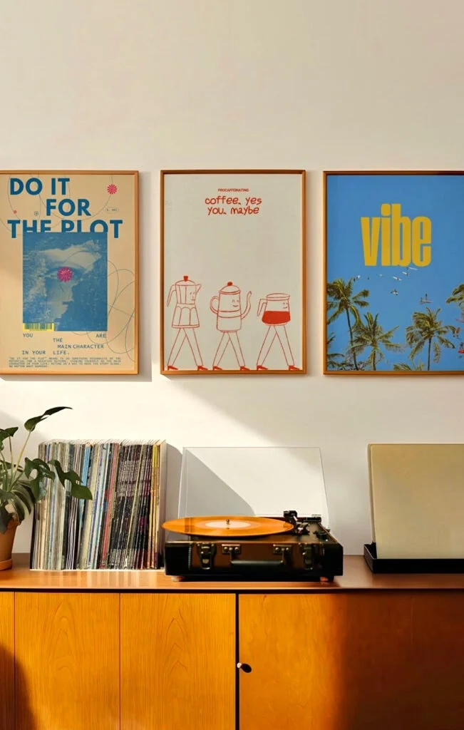 Three vertically aligned, framed indoor posters displayed on a wall above a wooden record console and turntable.