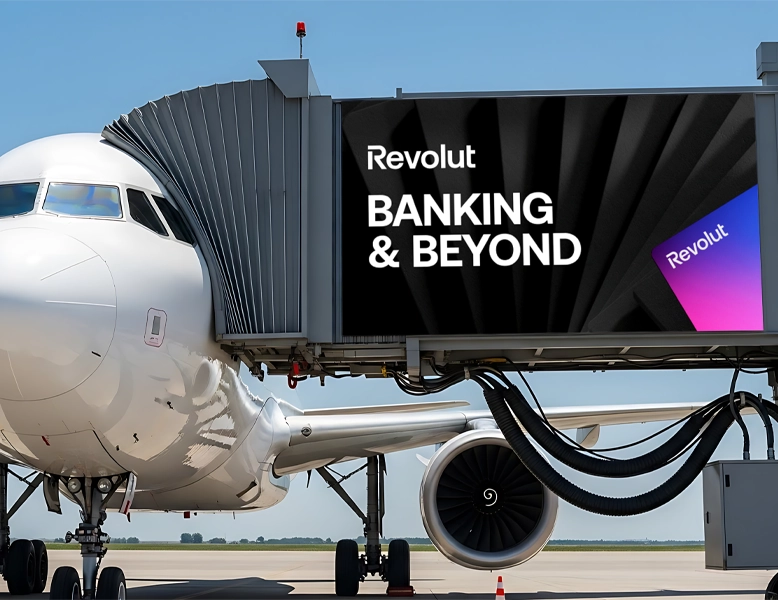 A large Revolut 'Banking & Beyond' advertisement on an airport jet bridge next to a white airplane.
