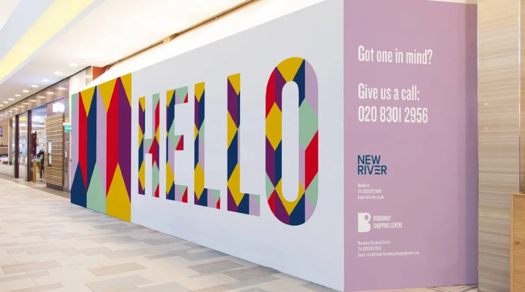 Large interior retail hoarding wall in a shopping mall featuring vibrant geometric patterns and the word "HELLO" in bold, patterned block letters.