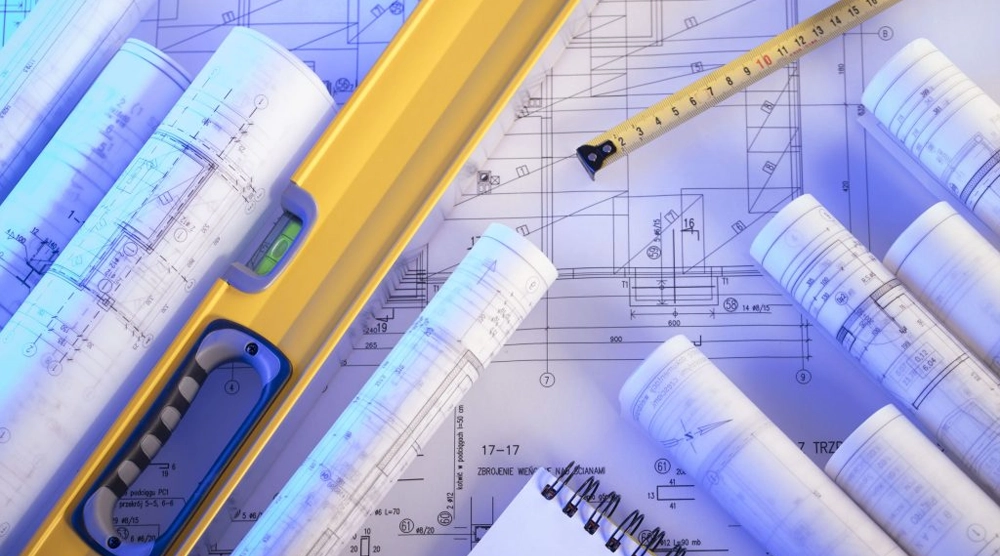 An overhead view of rolled architectural blueprints, a yellow spirit level, a measuring tape, and a spiral notebook under cool blue lighting.