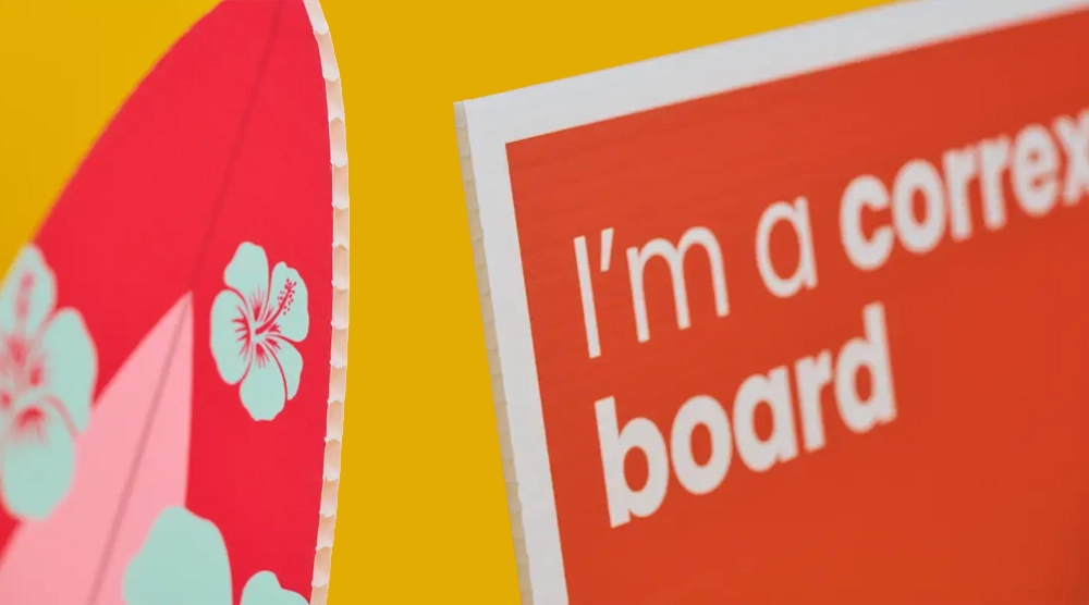 Close-up of custom-shaped Correx board printing featuring a red surfboard design with hibiscus flowers and a red rectangular sign.
