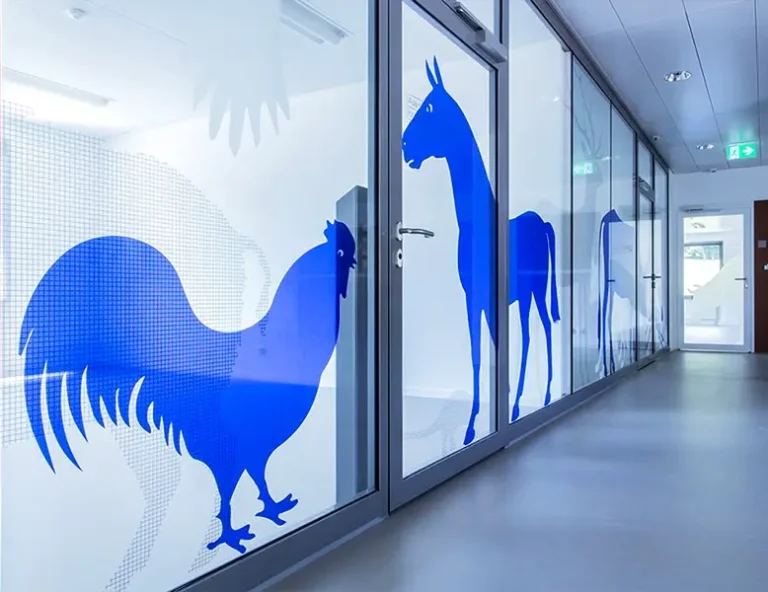 A long office hallway with glass partitions featuring large blue vinyl silhouettes of a rooster and a horse