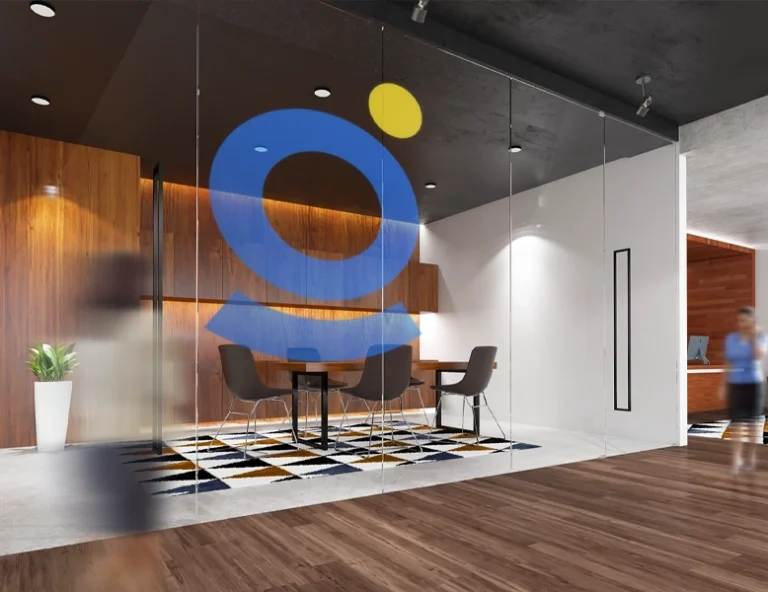 A large, translucent blue and yellow abstract geometric logo centered on a glass-walled office meeting room, with a modern interior featuring wooden panels and a patterned rug