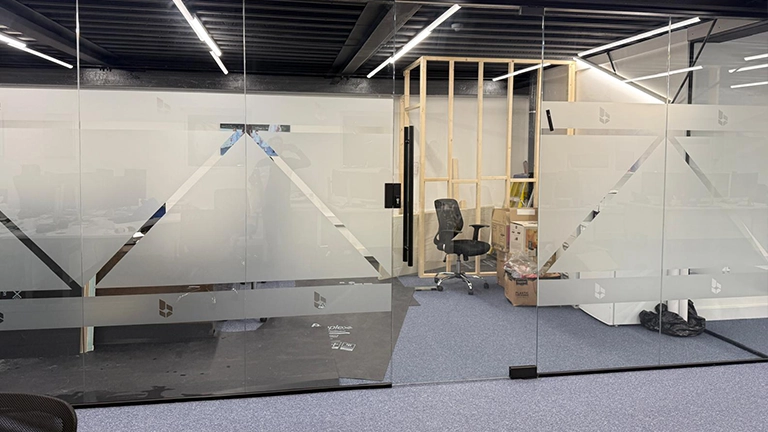 Large glass office partitions featuring etched-effect frosted vinyl with geometric patterns and company logos.