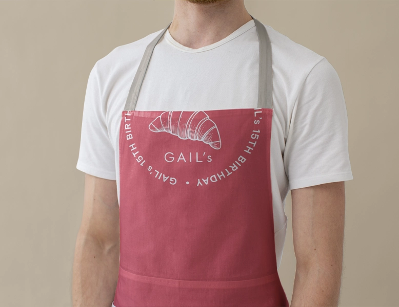 A man wearing a white t-shirt and a dusty rose-colored apron with a white silk-screened croissant illustration