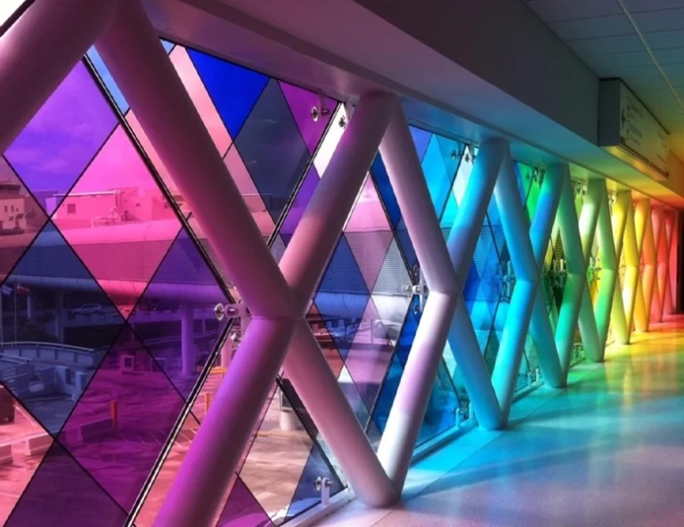 A large geometric window frame with diamond-shaped panes covered in vibrant, translucent pink, orange, and yellow vinyl film.