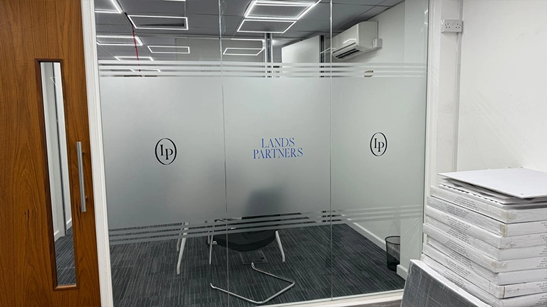 A glass office partition featuring a frosted vinyl privacy band with horizontal pinstripe borders and the "Lands Partners" corporate logo.