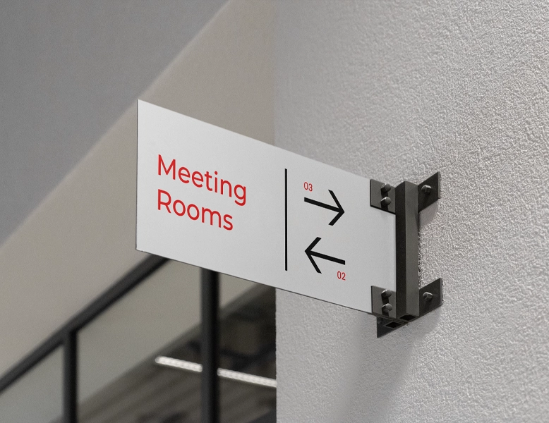 Modern white wall-mounted directional sign with red "Meeting Rooms" text and black arrows on a textured white wall.