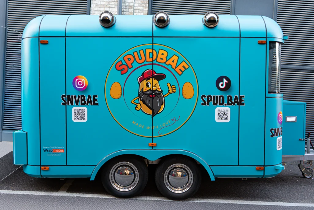 Vibrant turquoise full vinyl wrap for the Spudbae food trailer, featuring a cartoon potato mascot, social media handles, and QR codes.