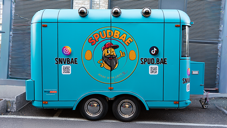 A vibrant turquoise catering trailer featuring the Spudbae logo and social media handles, showcasing high-quality trailer wrapping in London.